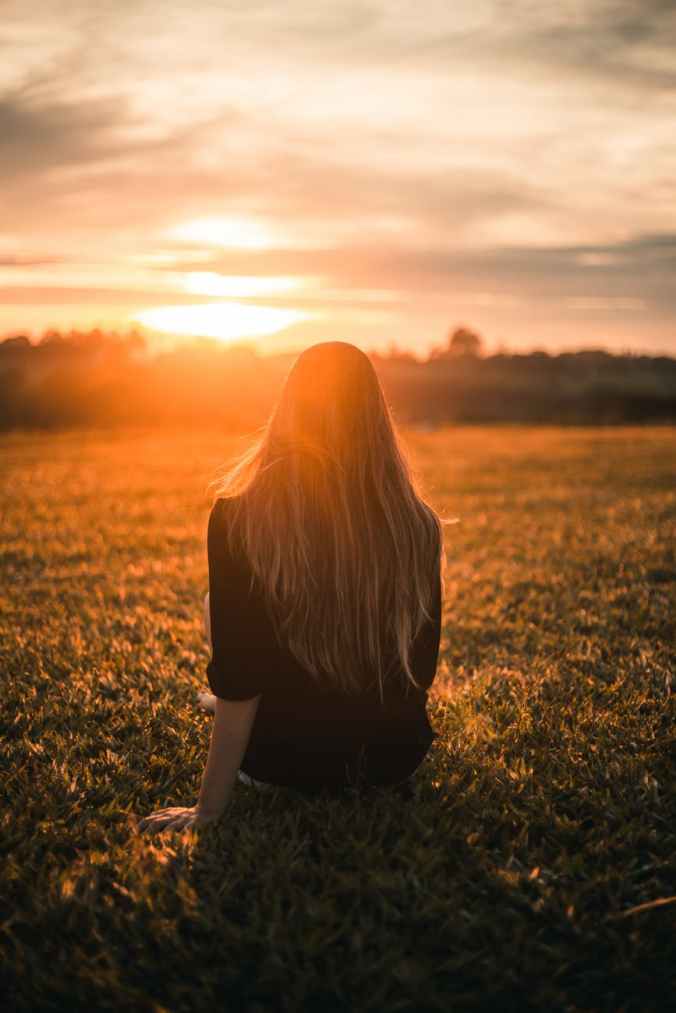 woman in black shirt sitting on grass during sunset